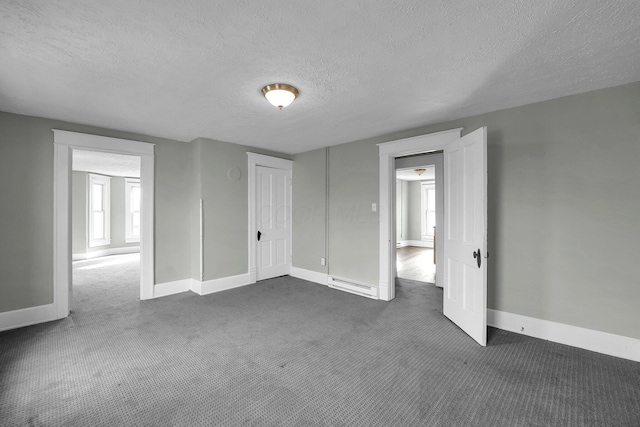 unfurnished bedroom featuring a baseboard heating unit, dark carpet, a textured ceiling, and baseboards