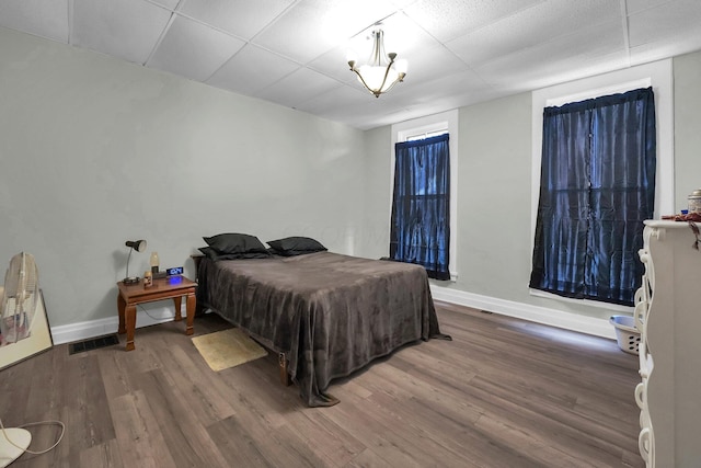 bedroom with visible vents, a drop ceiling, baseboards, and wood finished floors