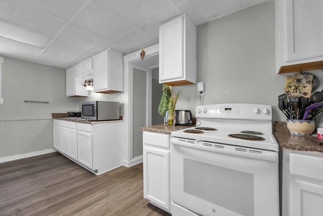 kitchen with stainless steel microwave, electric range, light wood-style floors, white cabinets, and baseboards