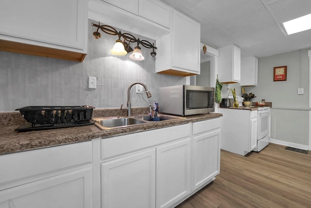 kitchen with electric stove, dark countertops, stainless steel microwave, white cabinets, and a sink