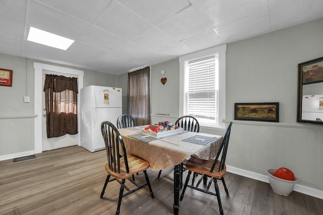 dining space with a paneled ceiling, a wainscoted wall, wood finished floors, visible vents, and baseboards