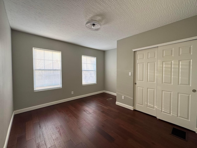 unfurnished bedroom with a closet, visible vents, dark wood-type flooring, a textured ceiling, and baseboards