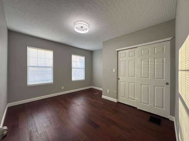 unfurnished bedroom featuring a closet, visible vents, dark wood-type flooring, a textured ceiling, and baseboards