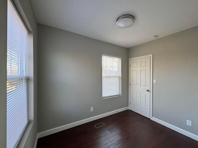 spare room featuring dark wood finished floors, visible vents, plenty of natural light, and baseboards