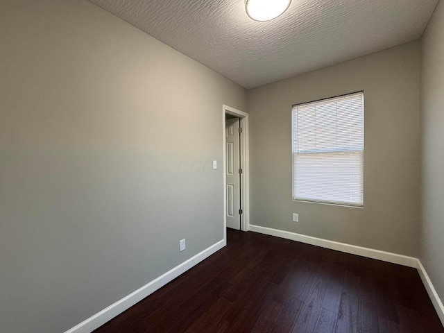 spare room with baseboards, dark wood finished floors, and a textured ceiling