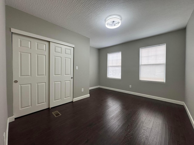 unfurnished bedroom with dark wood-style floors, a closet, visible vents, a textured ceiling, and baseboards