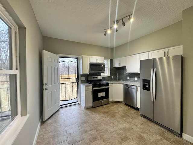 kitchen with decorative backsplash, light stone counters, stainless steel appliances, white cabinetry, and a sink