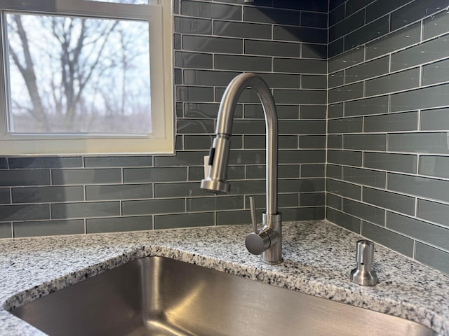 details featuring decorative backsplash, a sink, and light stone countertops