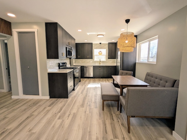 kitchen with decorative light fixtures, stainless steel appliances, light countertops, decorative backsplash, and a sink