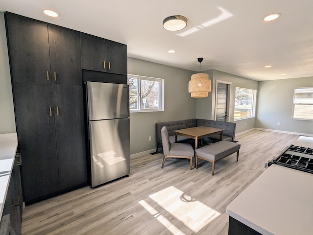 kitchen with light wood finished floors, light countertops, hanging light fixtures, freestanding refrigerator, and dark cabinetry