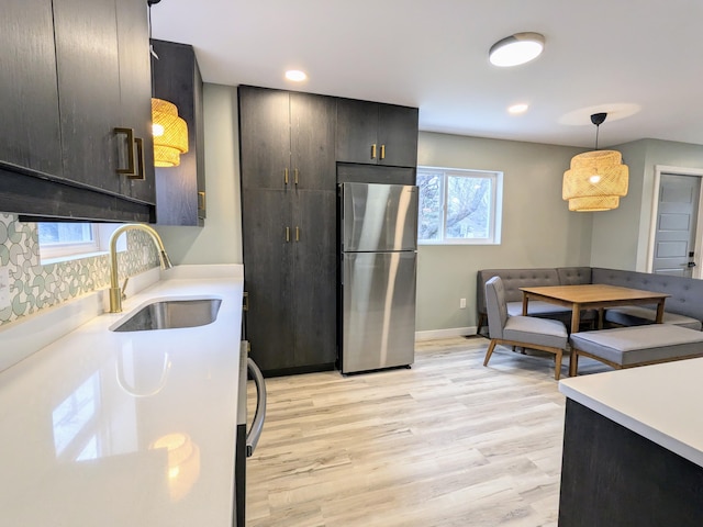 kitchen with pendant lighting, light wood finished floors, light countertops, freestanding refrigerator, and a sink