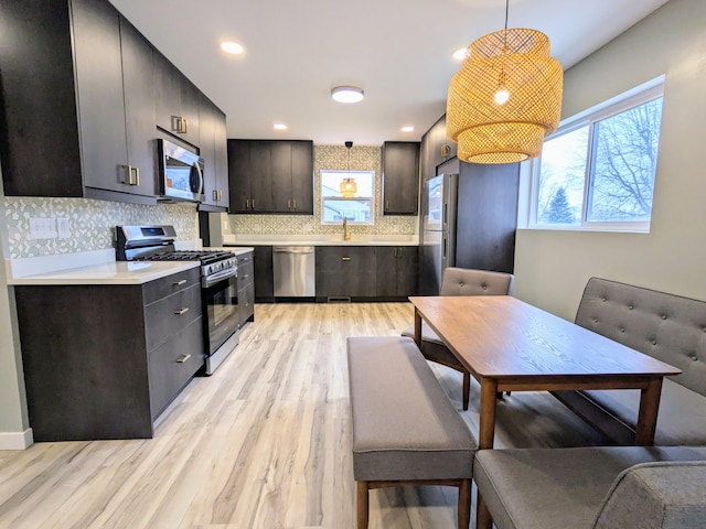 kitchen featuring stainless steel appliances, light wood-style floors, light countertops, tasteful backsplash, and pendant lighting