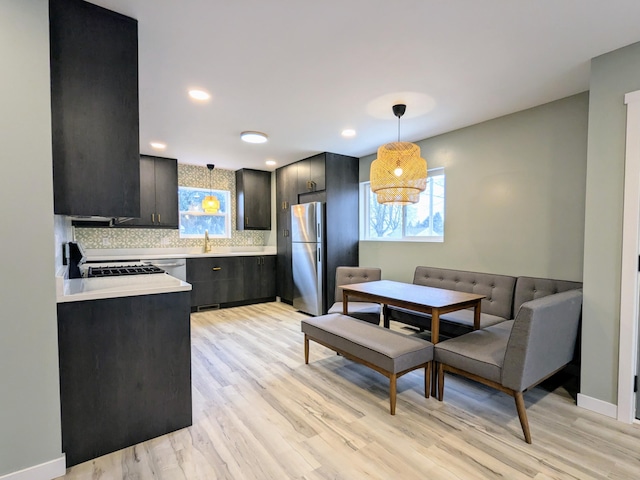 kitchen with light countertops, appliances with stainless steel finishes, backsplash, light wood finished floors, and decorative light fixtures