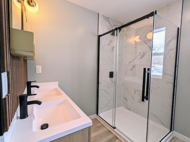 bathroom with wood finished floors, a sink, baseboards, a marble finish shower, and double vanity