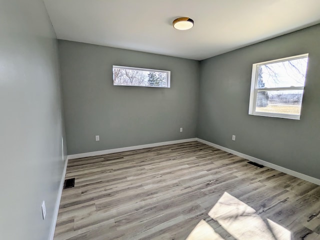 spare room featuring light wood-type flooring, visible vents, and baseboards