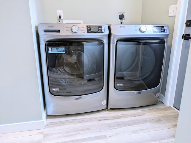 clothes washing area with laundry area, light wood finished floors, and washer and clothes dryer