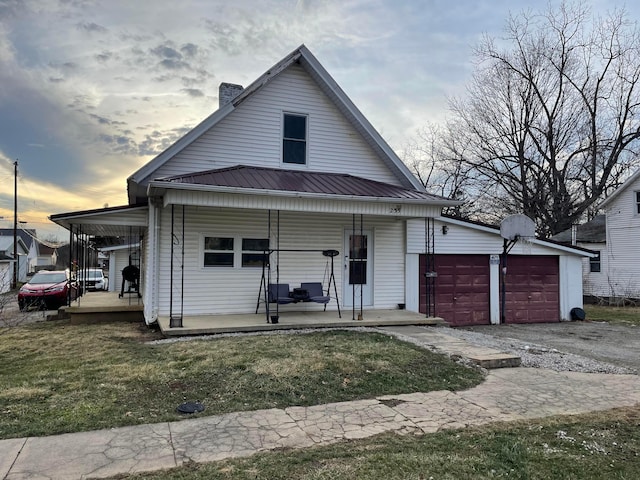 view of front of property with a porch, a front yard, metal roof, a garage, and driveway