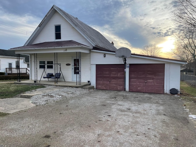 view of front facade featuring covered porch, metal roof, an attached garage, and driveway