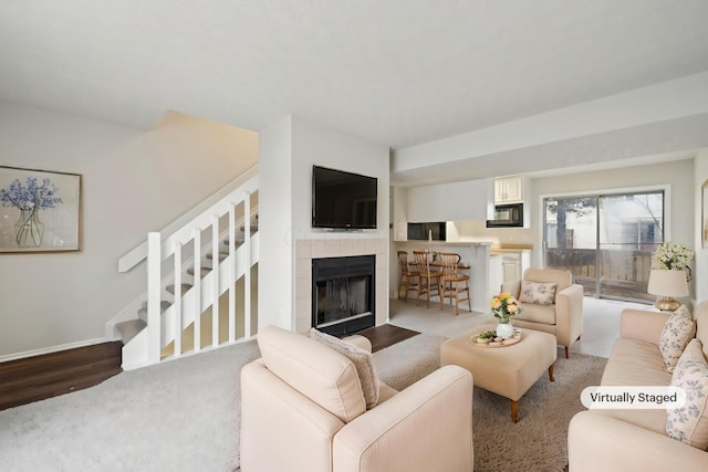 living room featuring baseboards, stairway, a tiled fireplace, and wood finished floors