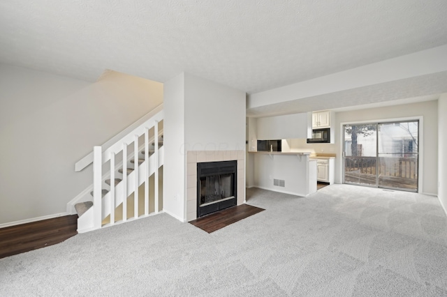 unfurnished living room with a textured ceiling, visible vents, stairs, dark carpet, and a tiled fireplace