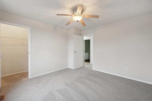 unfurnished bedroom with a spacious closet, a ceiling fan, carpet flooring, a textured ceiling, and baseboards