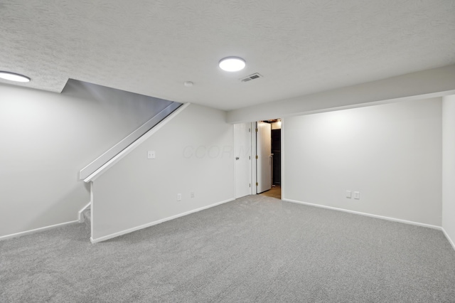 finished basement with a textured ceiling, carpet flooring, visible vents, baseboards, and stairs