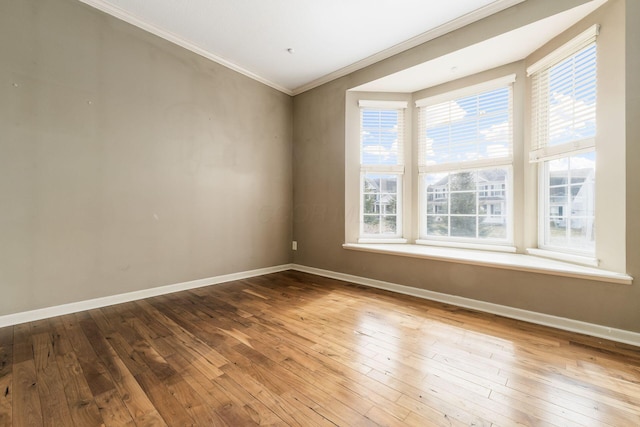 empty room featuring wood-type flooring, crown molding, and baseboards