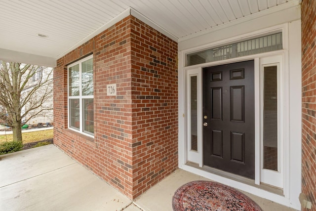 view of exterior entry featuring a porch and brick siding