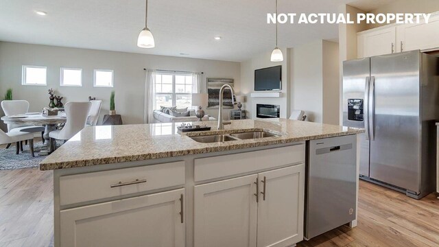 kitchen featuring white cabinets, a glass covered fireplace, appliances with stainless steel finishes, pendant lighting, and a sink