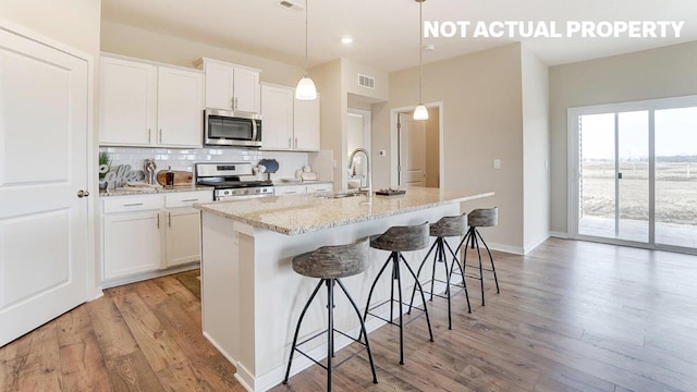 kitchen with light wood finished floors, tasteful backsplash, a center island with sink, appliances with stainless steel finishes, and a sink