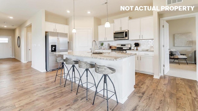 kitchen with light wood-type flooring, tasteful backsplash, appliances with stainless steel finishes, and a breakfast bar