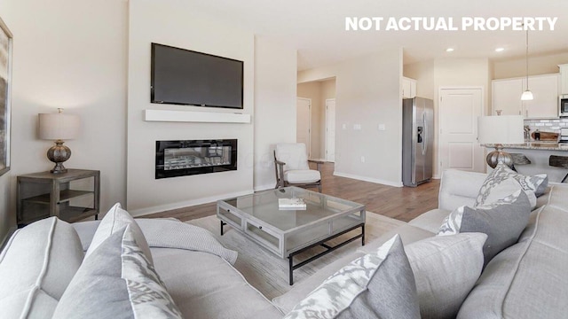 living area with baseboards, recessed lighting, a glass covered fireplace, and light wood-style floors