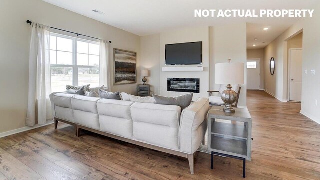 living area featuring light wood-style flooring, visible vents, baseboards, and a glass covered fireplace