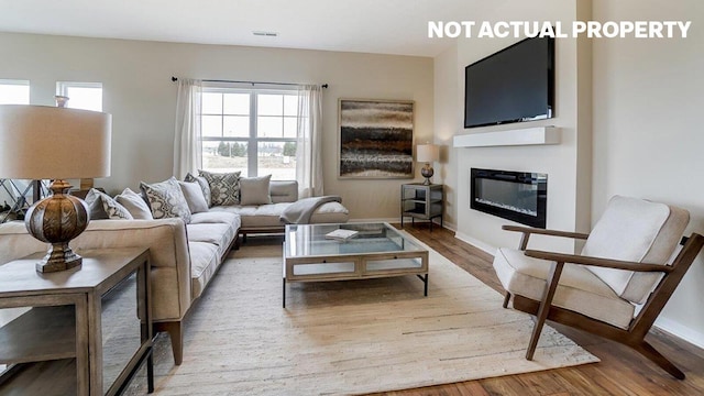 living area with baseboards, visible vents, wood finished floors, and a glass covered fireplace