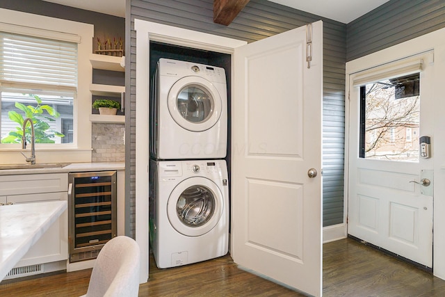 clothes washing area with wine cooler, laundry area, dark wood-style flooring, a sink, and stacked washer / drying machine