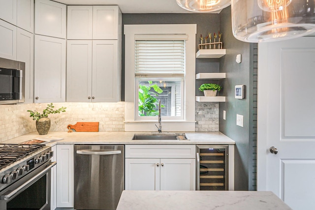 kitchen with beverage cooler, stainless steel appliances, a sink, and white cabinetry