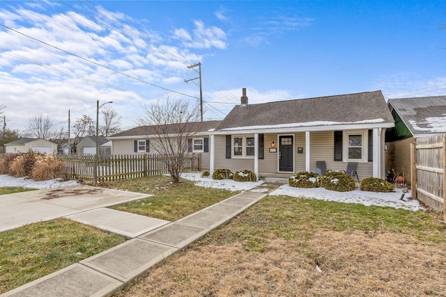 single story home featuring a porch, roof with shingles, fence, and a front lawn