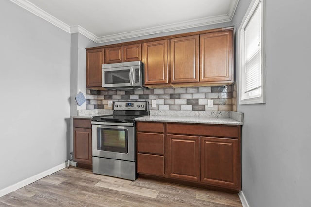 kitchen with baseboards, appliances with stainless steel finishes, ornamental molding, light countertops, and light wood-type flooring