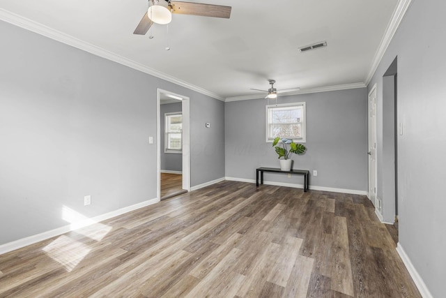 empty room with baseboards, visible vents, wood finished floors, and ornamental molding