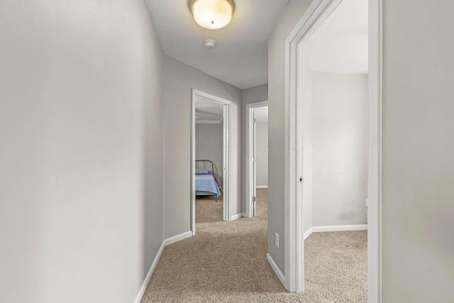 hallway with baseboards and light colored carpet