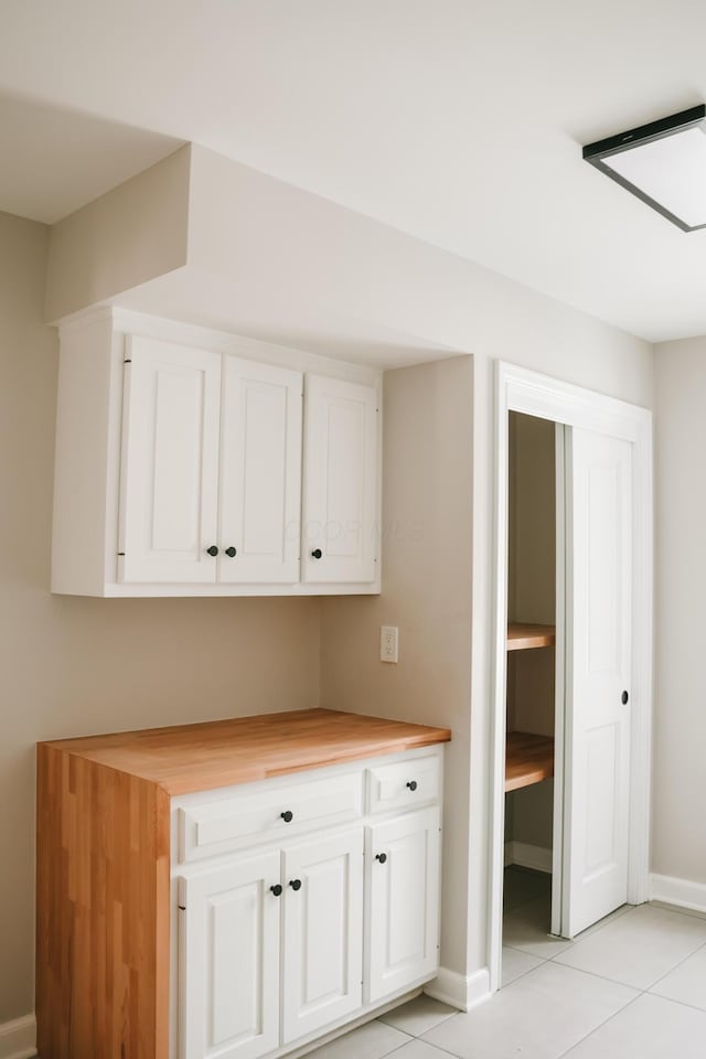 kitchen with baseboards, butcher block countertops, light tile patterned flooring, and white cabinets