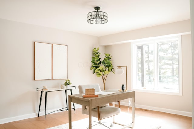 office space with light wood-style floors, visible vents, and baseboards