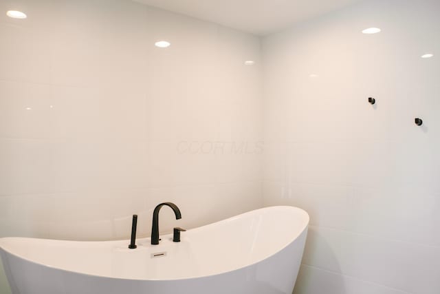 bathroom featuring a soaking tub, tile walls, and recessed lighting