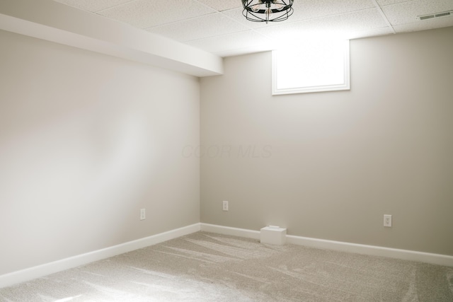 basement with a paneled ceiling, visible vents, baseboards, and light colored carpet