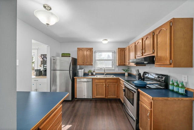 kitchen with dark countertops, brown cabinets, stainless steel appliances, under cabinet range hood, and a sink