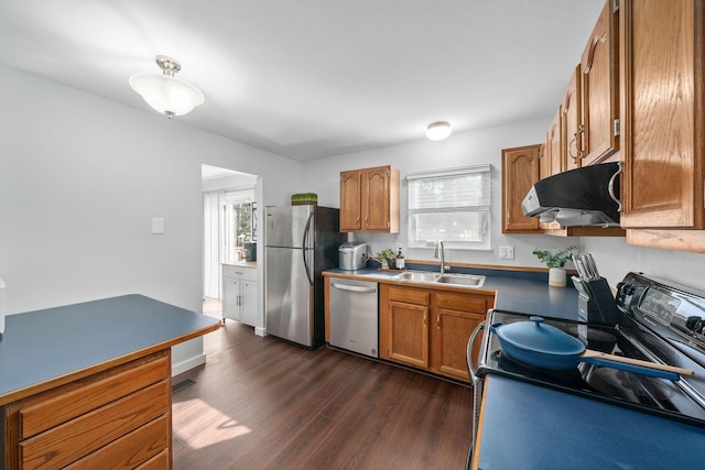 kitchen with dark wood-style flooring, brown cabinets, appliances with stainless steel finishes, a sink, and extractor fan