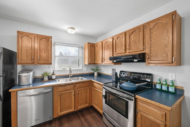 kitchen with under cabinet range hood, appliances with stainless steel finishes, brown cabinetry, and a sink