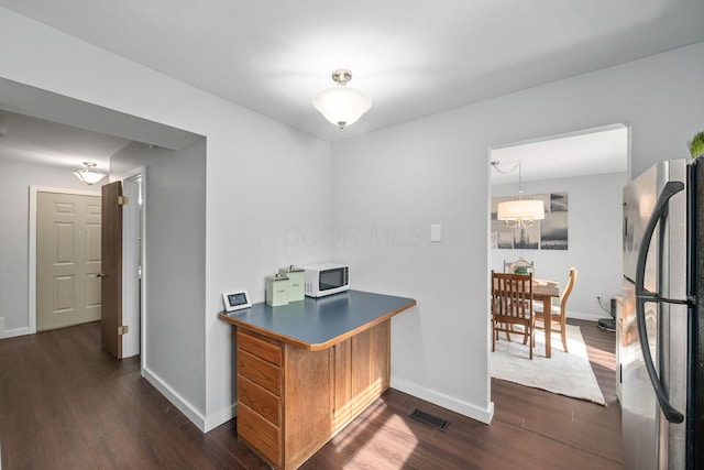 kitchen featuring white microwave, dark wood-style floors, visible vents, and freestanding refrigerator