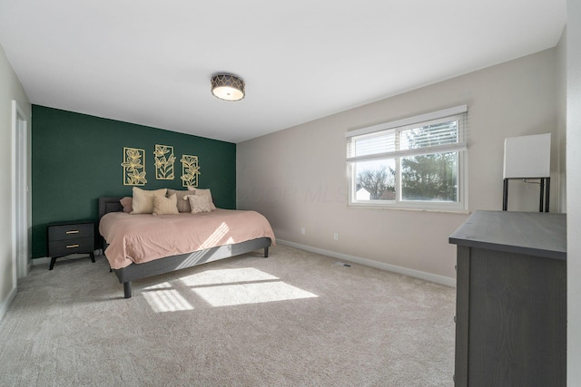 bedroom featuring an accent wall, baseboards, and light colored carpet