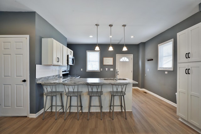 kitchen with stainless steel appliances, light stone countertops, a sink, wood finished floors, and a peninsula